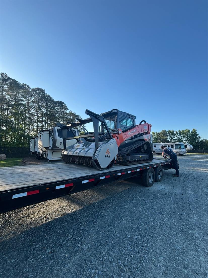 Justin strapping a Kubota track loader with an FAE mulching head to the gooseneck deck